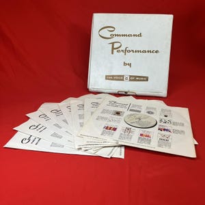 Puede incluir: Un conjunto de discos de vinilo vintage titulado "Command Performance by The Voice of Music". La caja blanca y las fundas de los discos presentan letras y gráficos dorados. Los discos están dispuestos sobre una superficie roja.