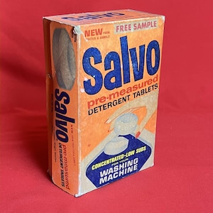 May include: A vintage orange and blue cardboard box of Salvo pre-measured detergent tablets. The front features the text Salvo, Free Sample, and Concentrated-Low Suds for your washing machine. A graphic shows a hand placing a white tablet into a machine.