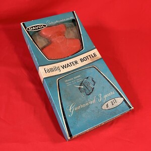 May include: A vintage Family Water Bottle in its original box. The box is light blue with the words "Family Water Bottle" in white. The bottle is red and visible through a clear window. The box also states "Guaranteed 3 years".