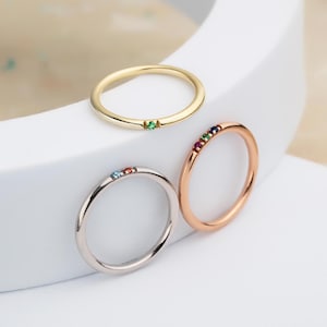 May include: Three simple gold, rose gold, and silver rings with small colourful gemstones set in the band.