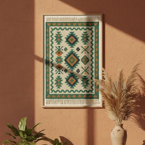 May include: Framed wall art featuring a geometric rug design. The rug has a cream-colored background with green, orange, and blue geometric patterns. The frame is a light wood color, and the artwork is displayed on a peach-colored wall.