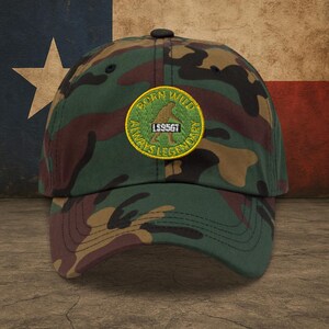 May include: A camouflage baseball cap with a green and yellow embroidered patch that reads "Born Wild Always Legendary" with a silhouette of a person and the text "LS95GT".