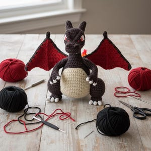 Peut inclure: Une peluche dragon crochetée marron foncé avec de grandes ailes rouges, un ventre crème et des griffes blanches. Le dragon a des yeux rouges et une petite flamme sur la queue. Il est entouré de pelotes de laine rouge et noire, de crochets et de ciseaux.