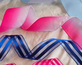 May include: Four decorative ribbons arranged in horizontal rows. The top ribbon is light blue with a subtle shimmer. The second is a pink ombre ribbon. The third is a blue and white striped ribbon. The bottom ribbon is pink and white striped.