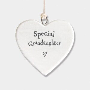 May include: A white heart-shaped ornament with the words "Special Granddaughter" in black script. A small heart symbol is below the text. The ornament hangs from a string.