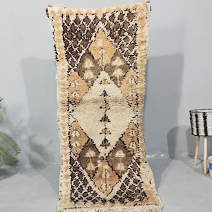 Könnte beinhalten: Ein rechteckiger Berber-Teppich in Beige und Braun mit einem Rautenmuster. Der Teppich hat eine zottelige Textur und eine cremefarbene zentrale Rautenform. Der Teppich wird vertikal präsentiert und zeigt sein kompliziertes Design und seine warme Farbpalette.