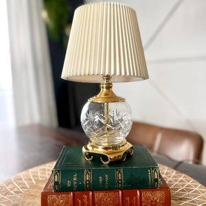 May include: A white ceramic mug with a black handle and the text "But First, Coffee" in a bold, black font. The mug is set against a blurred background, suggesting a cozy setting.