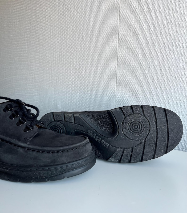 May include: A pair of black suede lace-up shoes with thick soles. The shoes have a classic design with visible stitching and a textured sole for grip. The brand name "GALLUS" is visible on the sole of one shoe.