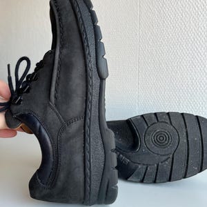 May include: Black leather shoes with a textured sole and laces. The shoes have a rounded toe and a dark navy blue accent on the heel. The sole is thick and sturdy, providing support and durability.