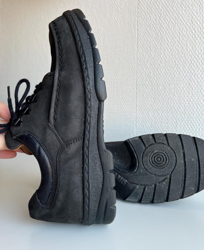 May include: Black leather shoes with a textured sole and laces. The shoes have a rounded toe and a dark navy blue accent on the heel. The sole is thick and sturdy, providing support and durability.