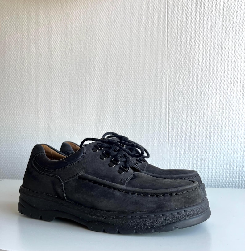 May include: A pair of black suede shoes with thick soles. The shoes have a lace-up design and a rounded toe. The soles are made of a durable material, and the shoes appear to be unworn.