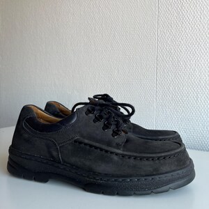 May include: A pair of black suede shoes with thick soles and black laces. The shoes have a classic, casual design, suitable for everyday wear. The shoes are displayed on a white surface.