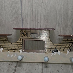 May include: A wooden wall-mounted coat rack shaped like a boat, featuring a brick-patterned cabin, a central rectangular frame, and four light blue pegs. The base is painted with white wave designs, and the top includes two small flat shelves.