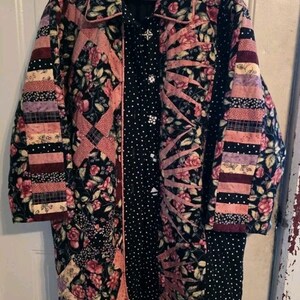 May include: A long-sleeved quilted coat featuring a patchwork design of black fabric with pink floral patterns, black fabric with white polka dots, and horizontal striped panels in shades of pink, purple, and black, finished with a collared neckline.