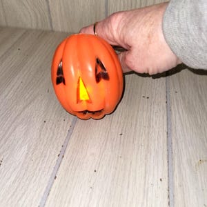 May include: Orange plastic Halloween pumpkin with black cut-out eyes and mouth. The pumpkin has a yellow light inside, creating a glowing effect. The pumpkin is a classic Halloween decoration.