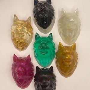 Pode incluir: Sete esculturas de cabeça de lobo de resina em várias cores, incluindo preto, branco, dourado, verde e rosa. Cada escultura tem um design geométrico e facetado.