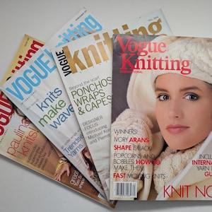 May include: A collection of four Vogue Knitting magazines arranged in a fan shape. The top magazine features a person wearing a cream-colored knit hat and scarf, with text including "Vogue Knitting," "Ivory Arans," and "Knit Now!" visible on the cover.