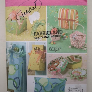 May include: A Simplicity 4320 sewing pattern envelope featuring various fabric gift bags, boxes, and containers. The cover displays images of finished projects with ribbons, bows, and colourful patterns, along with the text Fabricland and Wrights.