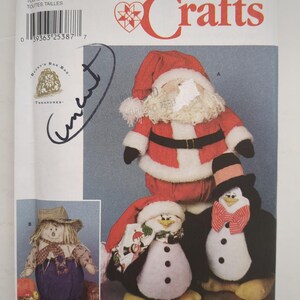 Peut inclure: Une pochette de patron de couture Simplicity Crafts 9953 illustrant une poupée Père Noël, deux poupées pingouins et une poupée épouvantail. L'emballage comporte des étiquettes textuelles, un code-barres et le mot uncut écrit à la main.