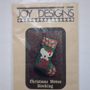 May include: A Joy Designs craft pattern package for a Christmas Mouse Stocking by designer Joy Nixon. The package features a green stocking with a white mouse wearing a red hat, accented with red, green, and white patchwork fabric patterns.