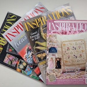 Op de afbeelding: Een verzameling van vier op elkaar gestapelde Inspirations handwerkbladen. Het bovenste tijdschrift heeft een roze omslag met een wit geborduurd kussen, bloemmotieven en tekst waaronder Grannies, Babies & Afternoon Tea en Inspirations.