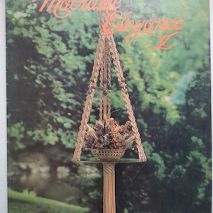May include: A craft instruction booklet titled Macramé Elegance II featuring a beige macramé plant hanger with wooden beads holding a bowl of dried flowers. The cover displays the text Macramé Elegance II and Belle Pensée with the code GS5M.