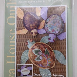 May include: A sewing pattern package titled Shell Shelters by Java House Quilts for zippered turtle cases in 10, 12, and 14 inch sizes. The cover features three fabric turtles with patterned shells and a small inset showing a zippered belly opening.