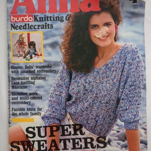 May include: A vintage magazine cover featuring the title "Anna" in large red letters. The cover model wears a blue and white speckled sweater. The magazine's headline reads "SUPER SWEATERS". Additional text includes "burda Knitting & Needlecrafts".