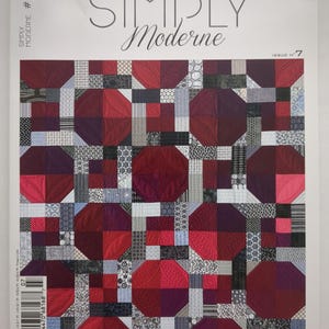 Op de afbeelding: De omslag van het tijdschrift "Simply Moderne" met een quiltontwerp. De quilt is een patchwork van rode, bordeauxrode en grijze geometrische vormen. De titel van het tijdschrift staat in een scriptletter, met het nummer van de uitgave zichtbaar.