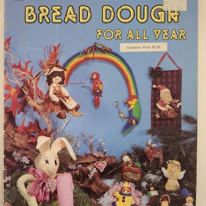 May include: A vintage craft book cover with the text "NEW AND EXCITING BREAD DOUGH FOR ALL YEAR." The cover features colorful bread dough figurines, including a bunny with a carrot, a doll, and a rainbow.