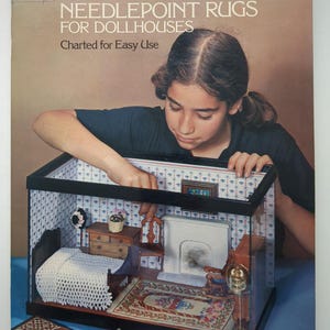 Puede incluir: Un libro de tapa blanda titulado Miniature Needlepoint Rugs for Dollhouses de Susan McBaine. La portada presenta una fotografía de una persona organizando muebles dentro de una habitación de casa de muñecas con papel tapiz estampado.
