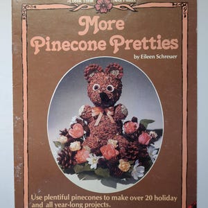 May include: A vintage book cover for "More Pinecone Pretties" by Eileen Schreuer. The cover shows a bear made of pinecones, surrounded by flowers and pinecones. The text says, "Use plentiful pinecones to make over 20 holiday and all year-long projects."