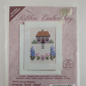 May include: A ribbon embroidery kit with a house design. The kit includes a notecard with a stitched image of a house with a brown roof, blue and pink flowers, and green bushes. The kit includes a card and envelope, measuring 10 x 13 cm.