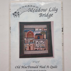 Puede incluir: Un patrón de costura para una colcha titulada Meadow Lily Bridge y Old MacDonald Had A Quilt de Denise McKenna. La portada muestra un diseño de colcha de 31 por 31 pulgadas con una escena de granja que incluye un granero rojo, una casa, un caballo, vacas y un espantapájaros.