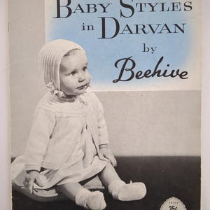 Puede incluir: Portada de libro de patrones de ropa de bebé vintage. La portada presenta a un bebé con gorro, suéter, vestido y calcetines de punto. El texto dice "Baby Styles in Darvan by Beehive". El precio es de 35 centavos.
