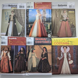 May include: A collection of six sewing pattern envelopes for historical costumes, including brands Butterick, Simplicity, and McCall's. Each envelope displays a photograph of a model wearing a period-style gown, with printed text identifying the pattern numbers.