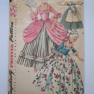 Puede incluir: Un sobre de patrón de costura vintage Simplicity, talla 8, con ilustraciones de dos vestidos de estilo histórico. Un vestido es rosa con falda a rayas y abanico, el otro es azul con falda floral. El texto incluye Simplicity Pattern 35c.