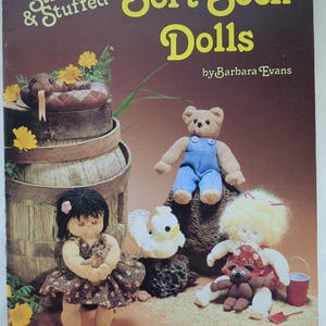 May include: A book cover titled "Soft Sock Dolls" by Barbara Evans, featuring various handmade sock dolls. The dolls include a bear in overalls, a girl in a floral dress, and a snake on a barrel. The cover also says "Stitched & Stuffed".