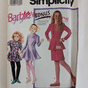 Peut inclure: Patron de couture Simplicity Barbie pour filles. L'emballage présente des illustrations de trois robes différentes. La couverture comprend le texte "Barbie Bonus" et "Transfert thermocollant inclus". La taille du patron est A (7-14).