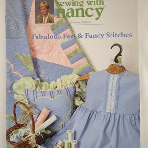 Könnte beinhalten: Ein Sewing with Nancy Lehrbuch mit dem Titel Fabulous Feet & Fancy Stitches #1517. Das Cover zeigt ein hellblaues Kleid auf einem Kleiderbügel, ein gestepptes Kissen mit Herzmotiv, einen Weidenkorb mit Garnrollen und Nancy Zieman.