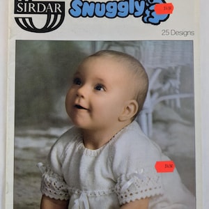 May include: Vintage Sirdar knitting pattern booklet titled "Snuggly" featuring a baby in a white knitted outfit. The cover includes the Sirdar logo and the text "Snuggly" in blue. The booklet advertises 25 designs.