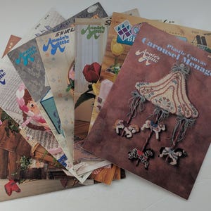 Peut inclure: Une collection de livrets de modèles d'artisanat Annie's Attic présentant divers designs, dont un projet de ménagerie de carrousel en canevas plastique sur la couverture. Les livrets affichent des illustrations colorées de projets finis.