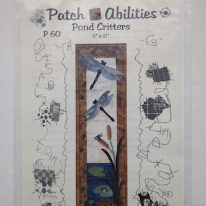 Op de afbeelding: Een Patch Abilities Pond Critters naaipatroon in een doorzichtige plastic zak. De hoes toont een verticaal quiltontwerp met twee blauwe libellen, lisdodden, waterlelies en een schildpad. De tekst luidt Patch Abilities, Pond Critters, P 60, 15,24 cm x 53,34 cm.