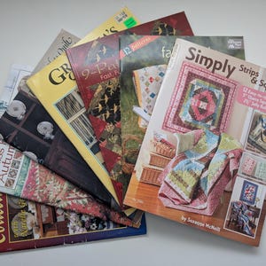 May include: A collection of eight softcover quilting instruction books fanned out, featuring various colourful quilt designs on the covers. Titles include Simply Strips & Squares, 9-Patch, and Miss Rosie's Autumn, showcasing patterns, fabric blocks, and finished quilts.