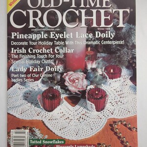 Puede incluir: La portada de la revista "Old-Time Crochet" presenta un tapete de ganchillo blanco con candelabros rojos y un centro de mesa. El texto incluye "Pineapple Eyelet Lace Doily" y "Winter 1999". La revista promueve proyectos de ganchillo de invierno.
