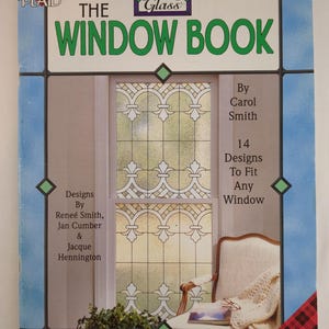 May include: A book titled "The Window Book" by Carol Smith, featuring 14 designs to fit any window. The cover has a blue border with green diamond accents and a stained-glass window design.