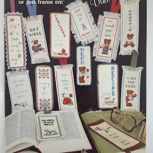 Könnte beinhalten: Eine Sammlung von bestickten Lesezeichen mit verschiedenen Designs und Texten, darunter "Get Well" und "Teachers". Die Lesezeichen zeigen Teddybären, Herzen und andere Motive mit ausgefransten Kanten und bunten Bändern. Das Bild zeigt auch offene Bücher und eine Brille.