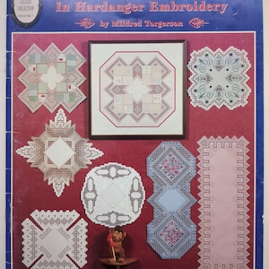 May include: A softcover book titled A Little Bit of Norway In Hardanger Embroidery by Mildred Torgerson, compiled by Susan L. Meier and Rosalyn K. Watnemo. The cover features various white and colored Hardanger embroidery patterns on a red background.
