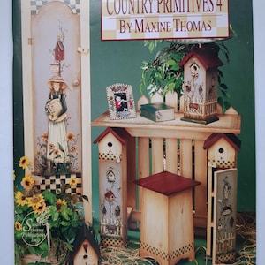 May include: The cover of "Country Primitives 4 by Maxine Thomas" features a painted scene with a wooden cabinet, birdhouses, and a small table. The birdhouses have red roofs and decorative details. The scene is set against a green background.