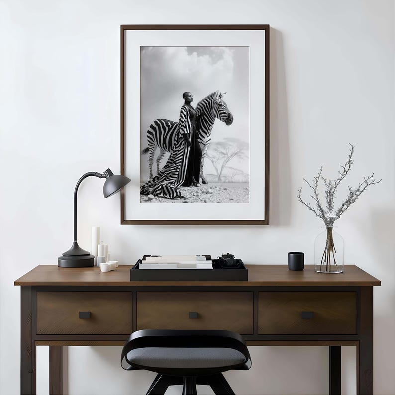 May include: Monochrome framed print featuring a person in a long dress posing with a zebra. The print is on a dark brown desk with a black lamp, candles, and a decorative tray.